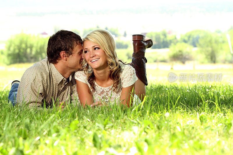 男人躺在草地上，对着女伴耳语