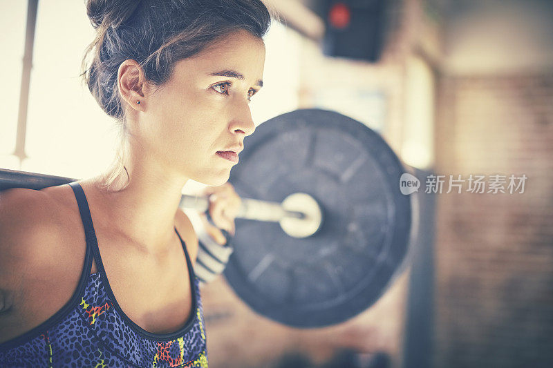 坚定的女人在健身房用杠铃锻炼的特写