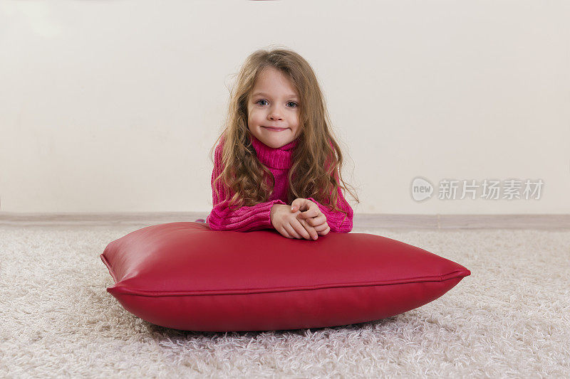 小女孩微笑着躺在红垫子上