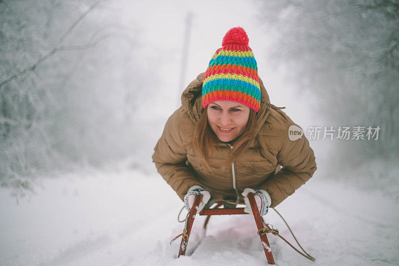 快乐的年轻女子在一个快速的雪橇骑下冰冷的斜坡