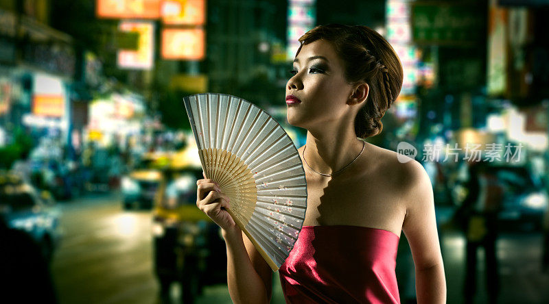 年轻的中国女子晚上在市中心给自己扇风
