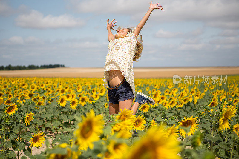 快乐的女人跳跃着双臂伸展在向日葵地中间