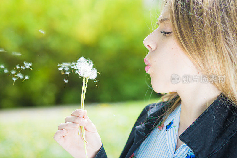 一个快乐的年轻金发女人吹蒲公英的特写