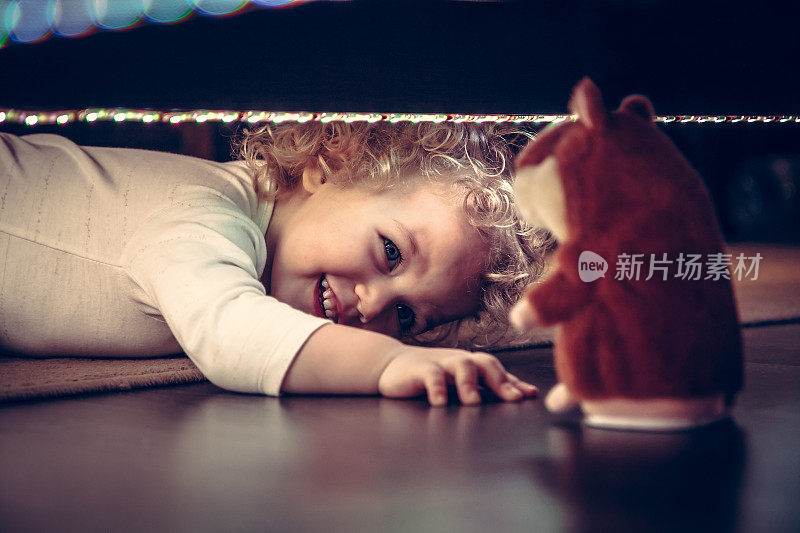 有趣可爱的微笑婴儿玩捉迷藏在床下与玩具仓鼠在复古风格