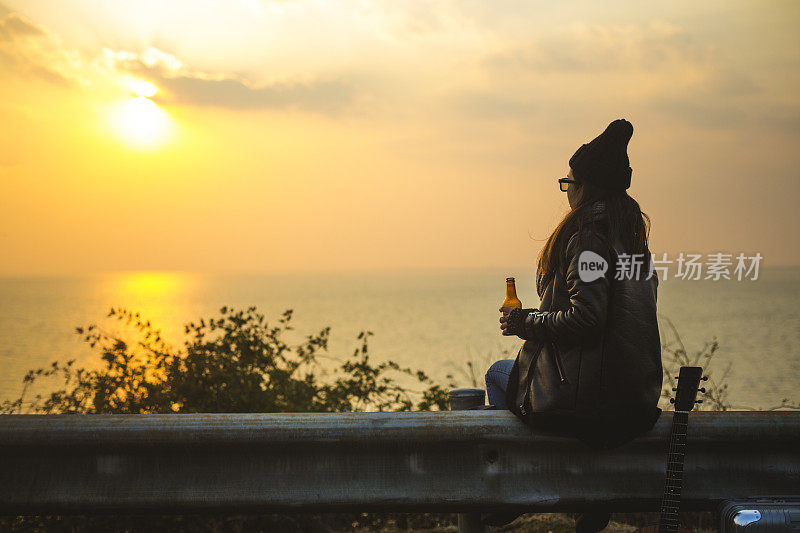 夕阳西下，年轻女子喝着啤酒