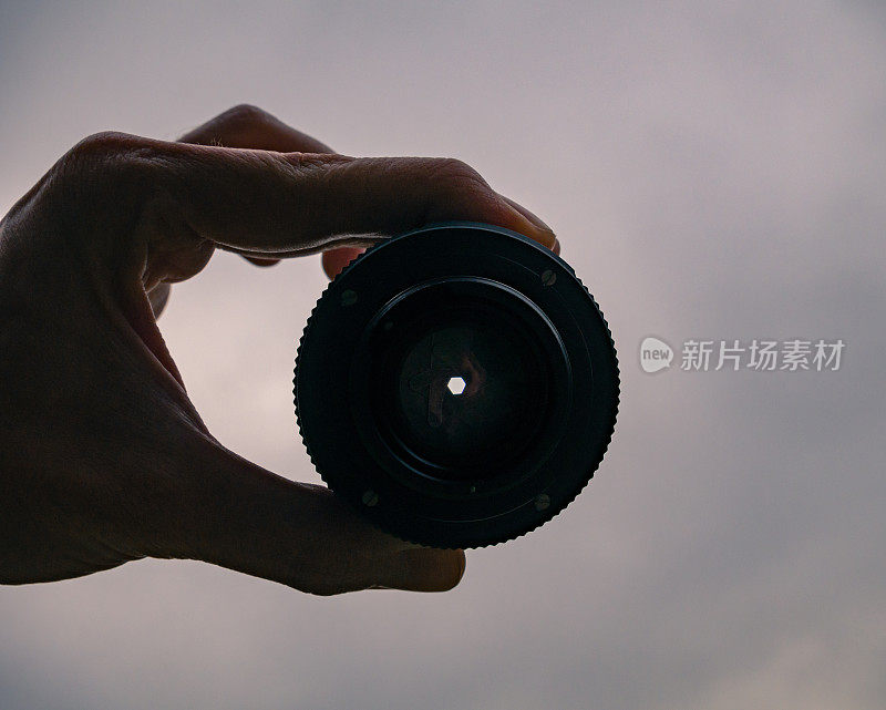 男性手中拿着一个老式相机镜头在空中。背景中的天空。
