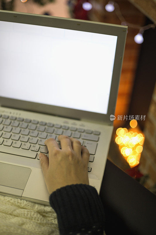 在一个寒冷的冬天，一个年轻女子坐在家里的壁炉前，用笔记本电脑工作。
