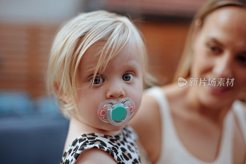 一个婴儿女孩与奶嘴和她的妈妈在背景的特写