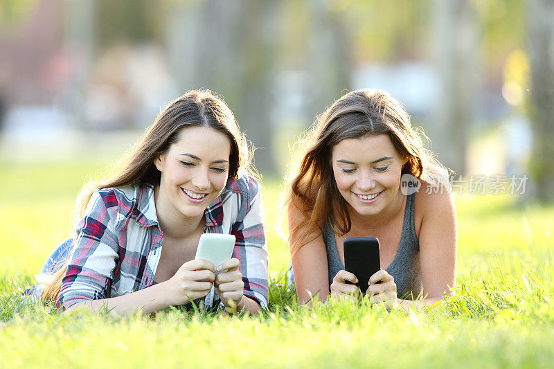 两个朋友在草地上用他们的智能手机