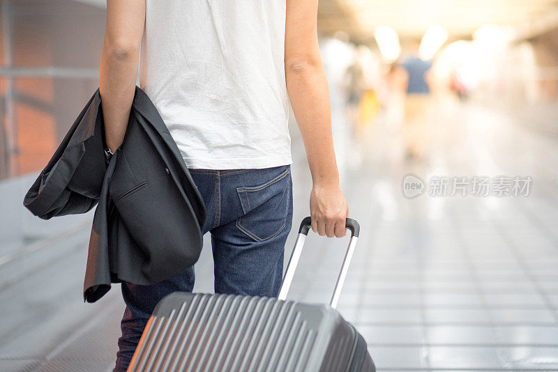 年轻的亚洲人拿着西装和行李走在机场候机楼里