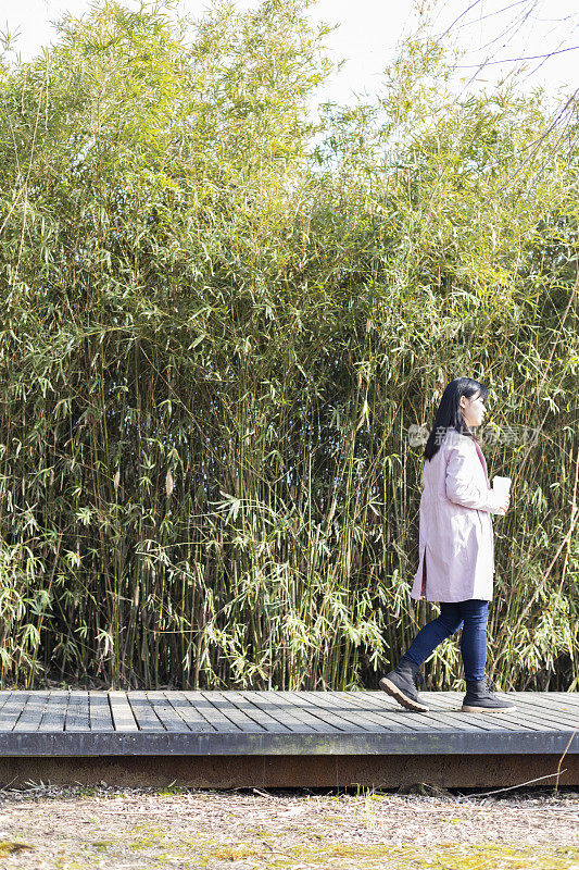 年轻女性拿着一次性杯子走在公园小径上