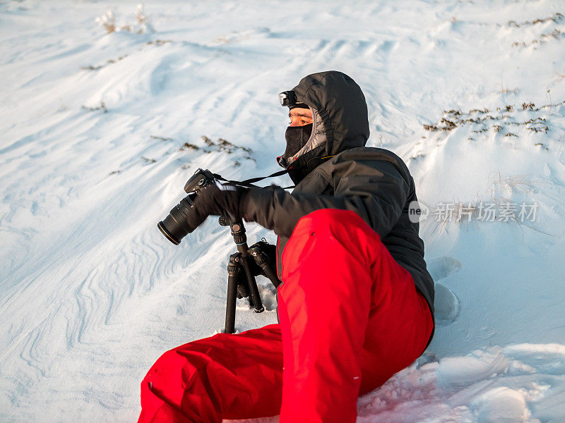 业余摄影师躺在雪地里，手里拿着数码相机