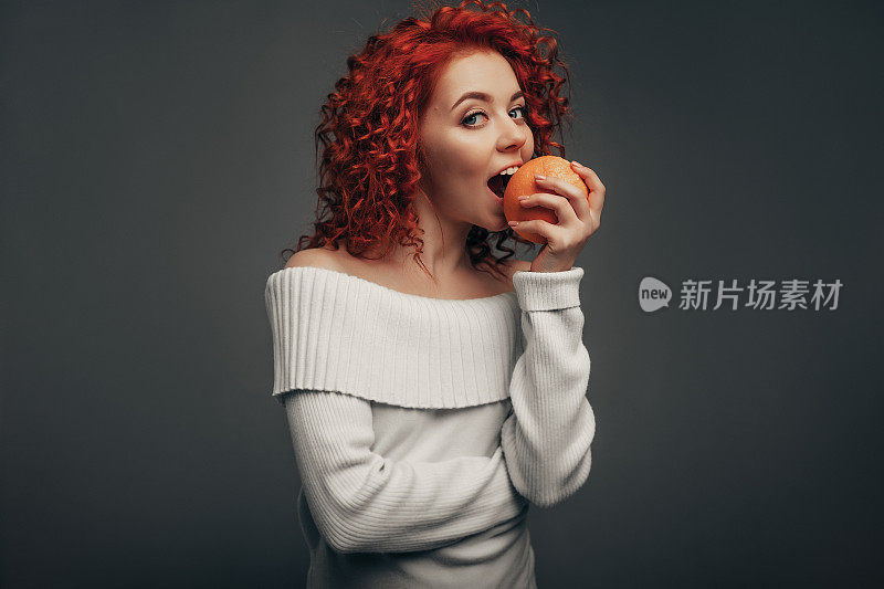 可爱的红发卷女孩咬了一个橙子