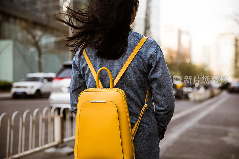 年轻女子背着背包，站在城市的街道上