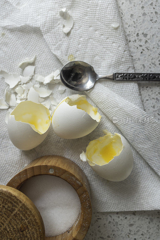 厨房桌子上放着三个鸡蛋壳和一个木制盐瓶和一个勺子。