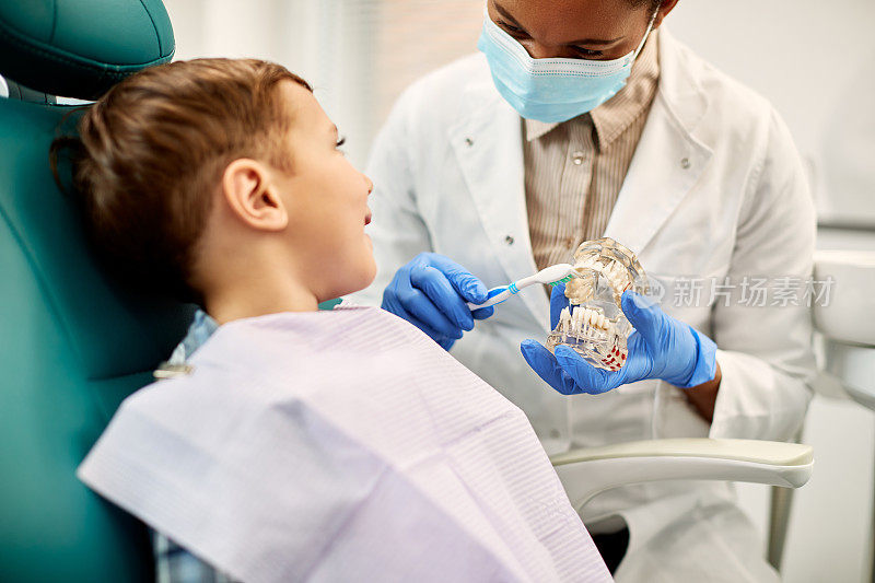 牙科医生教男孩如何正确刷牙在牙科预约特写。