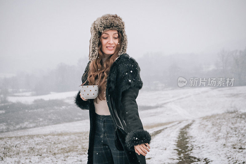 站在雪地上拿着一杯茶的年轻女子