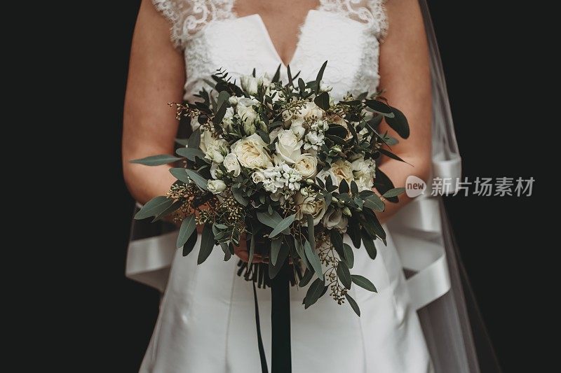 新娘身穿白色婚纱，手持黑色背景下美丽的花束