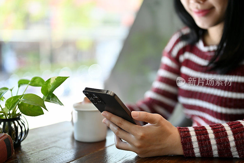 美丽的亚洲女子在咖啡店放松时使用她的智能手机。裁剪图像