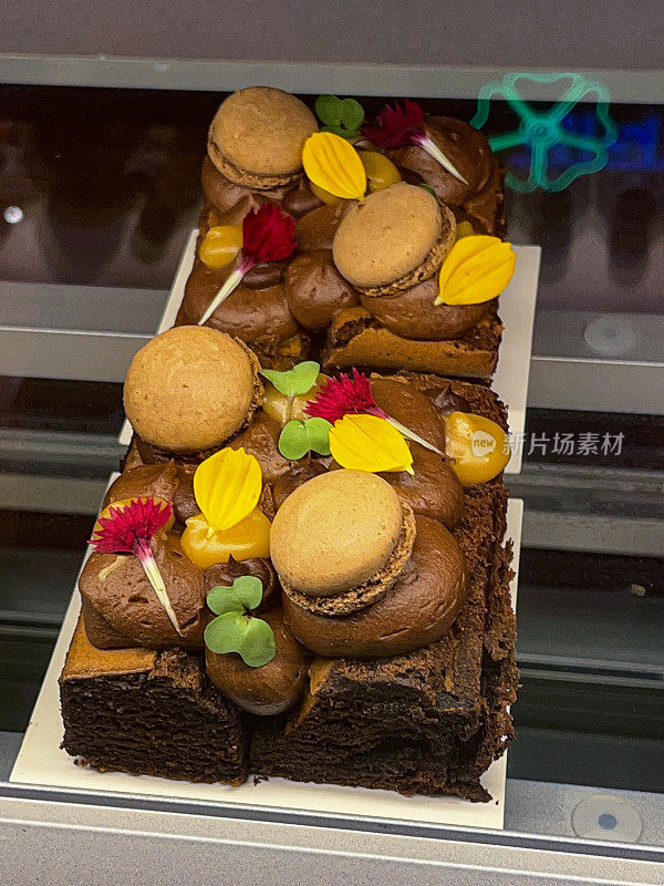 图片展示了美味的巧克力软糖布朗尼，托盘烘焙蛋糕，烘烤和顶部的马卡龙和花瓣，在白色盘子，面包店展示照片与黑色背景