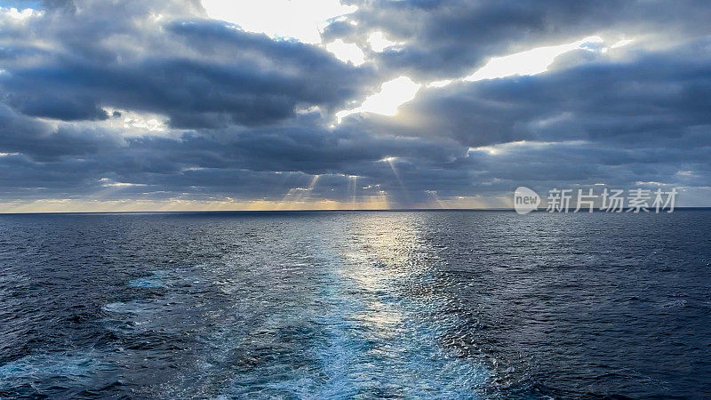 在戏剧性的日落云景下，太平洋上一艘大船的螺旋桨冲洗