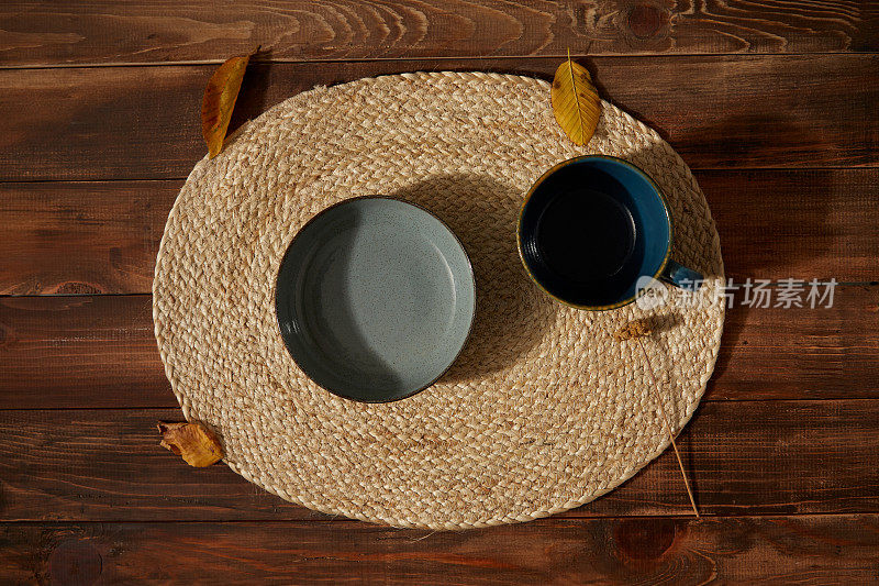 小盘子下面放柳条餐垫。木制背景上的秋叶。