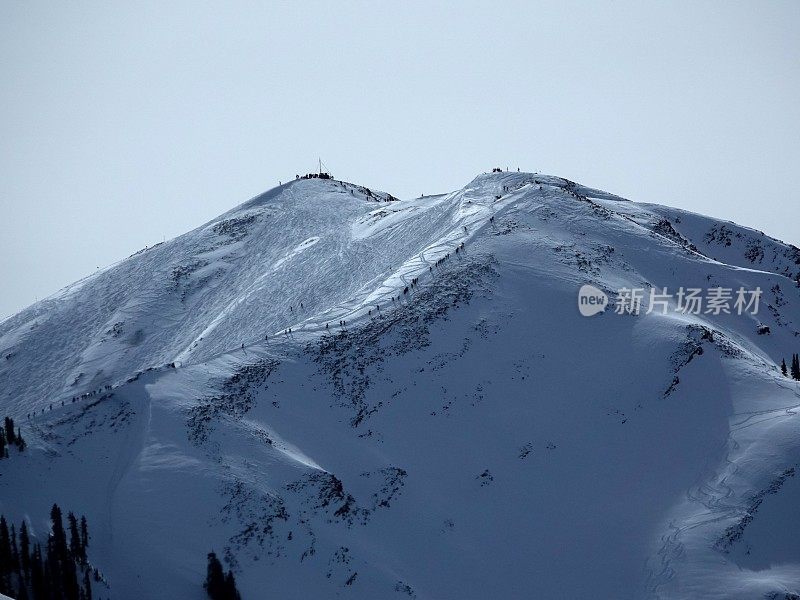 长焦视图数十名滑雪者和滑雪板徒步到12392英尺的高地峰滑雪碗。