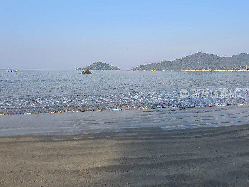 印度果阿邦Palolem海滩的海岸线，海浪拍打着海滩，船在地平线上，湛蓝晴朗的天空