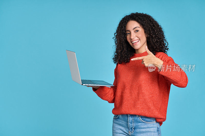 年轻快乐兴奋的拉丁女人指着笔记本电脑孤立的蓝色。