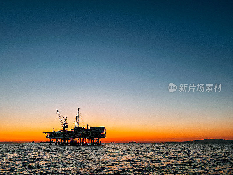 亨廷顿海滩海岸附近的一个海上石油钻井平台的广角低角度日落照片