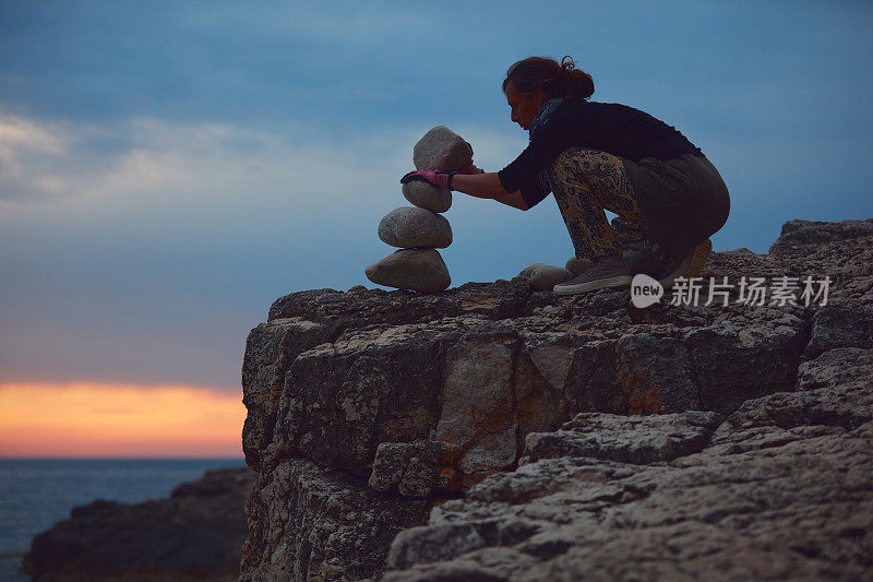 一个女人的剪影平衡岩石和石头在海洋海岸在日落日出时间。