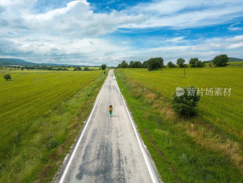 春天里，年轻的背包旅行者女孩走在美丽的乡间小路上