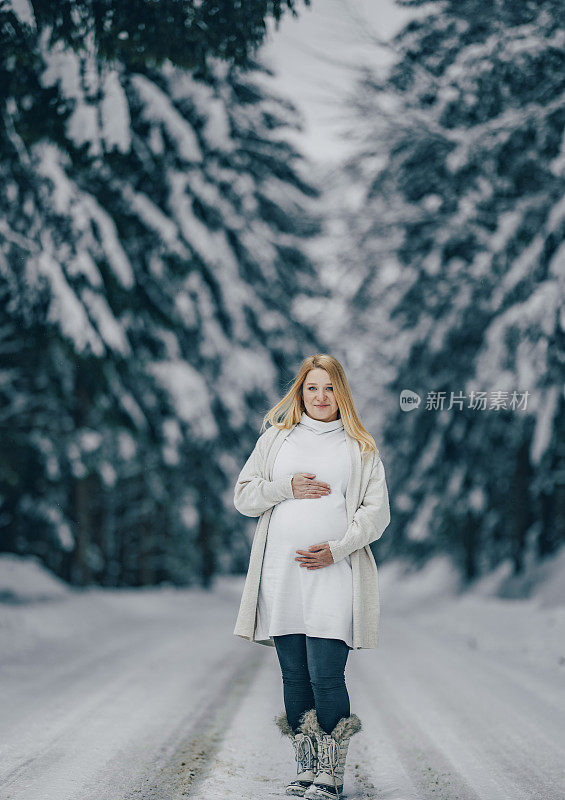 一个孕妇在雪林里摸自己的肚子