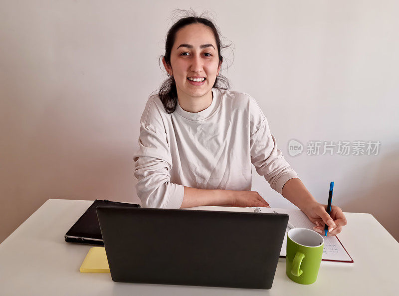 漂亮的年轻女子在家里用笔记本电脑和ipad，戴着耳机和一杯饮料