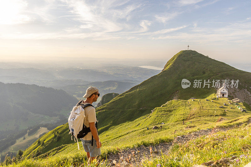 一名男子在日出时沿着长满草的山脊徒步