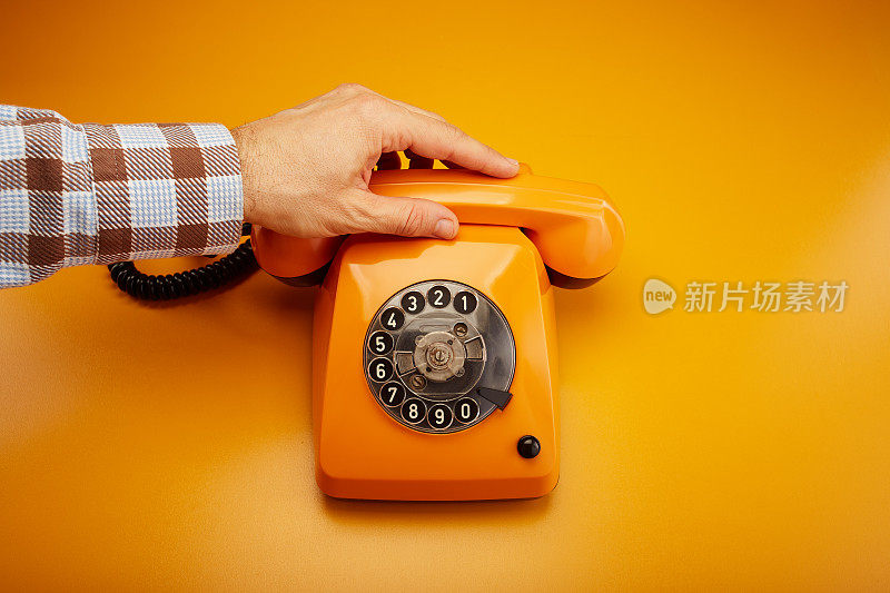 接到一个电话。拿着一个老式的电话听筒。一个橙色的复古电话接收机手持手持桔黄色的背景