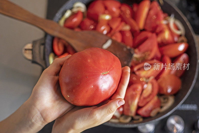 女孩用双手在煎锅上拿着一个粉红色的西红柿。flatlay