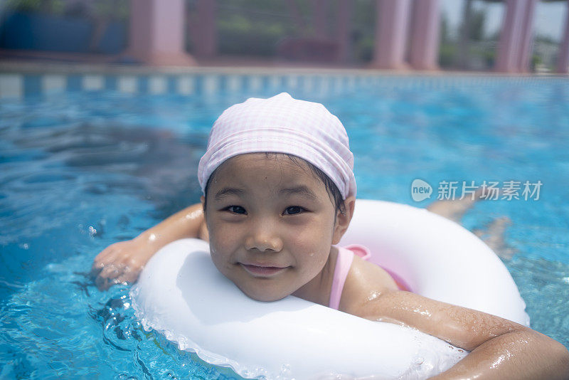 小女孩戴着游泳圈在游泳池里游泳