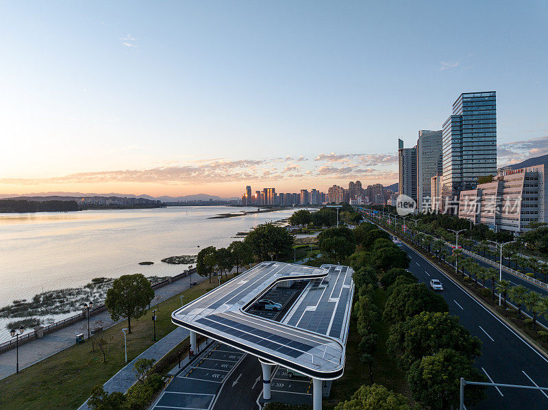 黄昏的水边城市绿化带，屋顶上有太阳能电池板的停车场