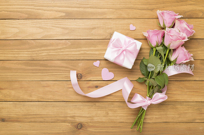 粉红色玫瑰与心和礼盒木制背景，俯视图。