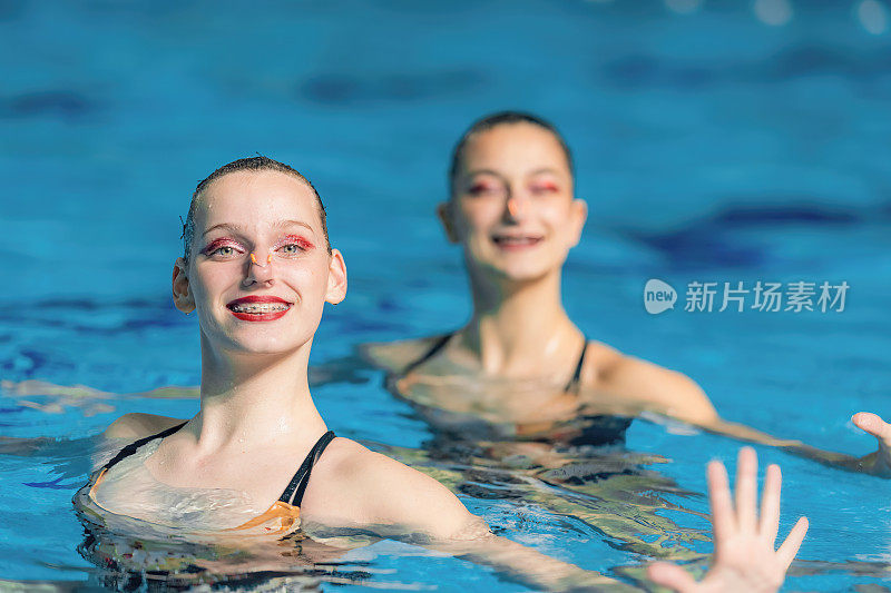 一个女子双人花样游泳表演，流畅的动作和同步的优雅创造了一个迷人的舞蹈在游泳池
