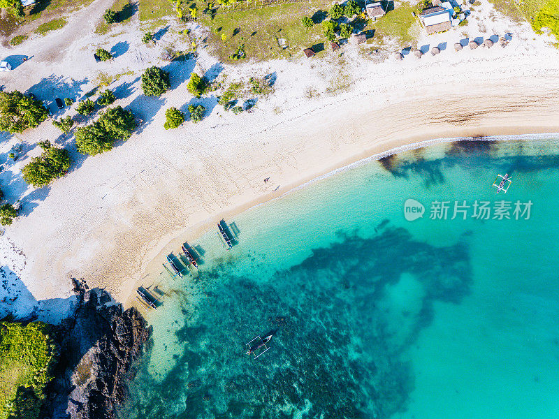 鸟瞰宁静的海滩，清澈的海水，船只和龙目岛的绿色植物。