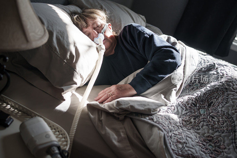 患有睡眠呼吸暂停的中年妇女躺在床上，戴着CPAP(持续气道正压通气)机辅助睡眠
