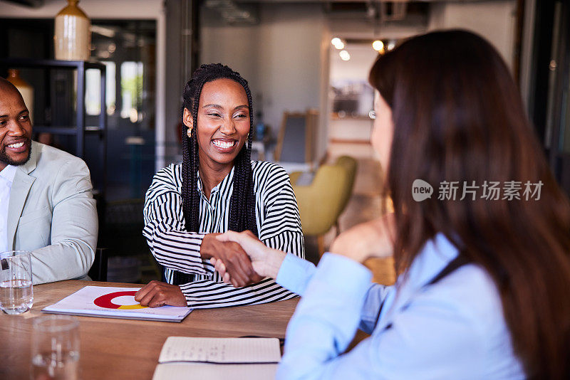 两个微笑的年轻女商人在办公室会议上握手