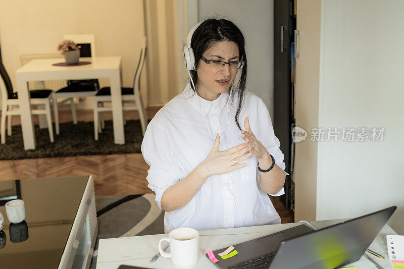 工作中的情绪。一位戴着耳机的沮丧的年轻女子正带着很大的压力在家办公室工作。现代虚拟理财顾问和咨询。远程办公，商务，自由职业者，网上购物，电子学习。