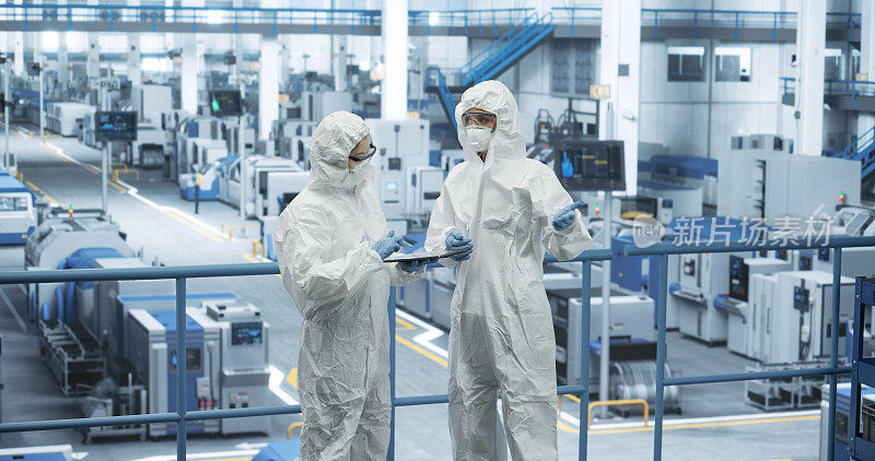 女工们在工厂里穿着全身的聚丙烯工作服。专家使用平板电脑，讨论自动化工作流程。保护员工免受有害物质侵害