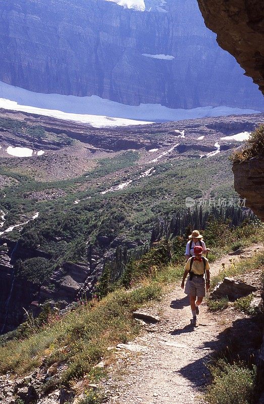 在蒙大拿冰川国家公园的格林内尔冰川下，徒步旅行者沿着陡峭的小路，背景是极端的地形
