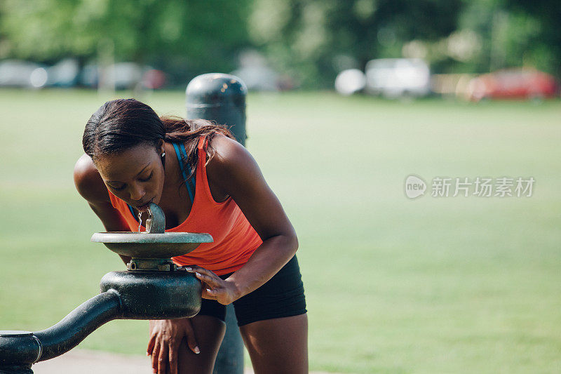 女慢跑者在城市公园喝水