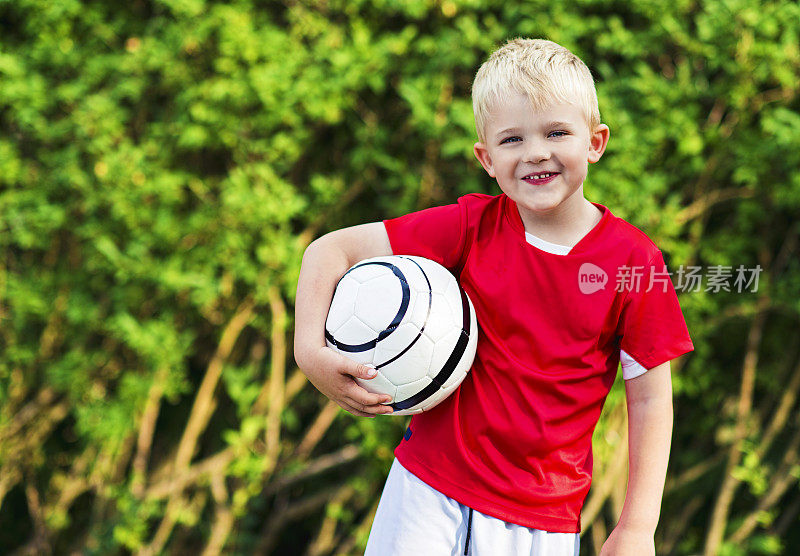 穿着足球衫的小男孩拿着一个足球