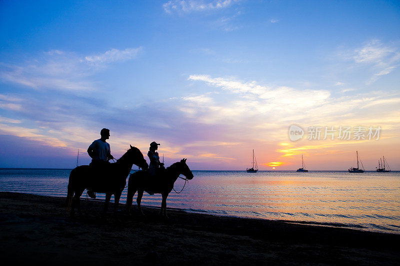 一对情侣在日落时分的海滩上骑马